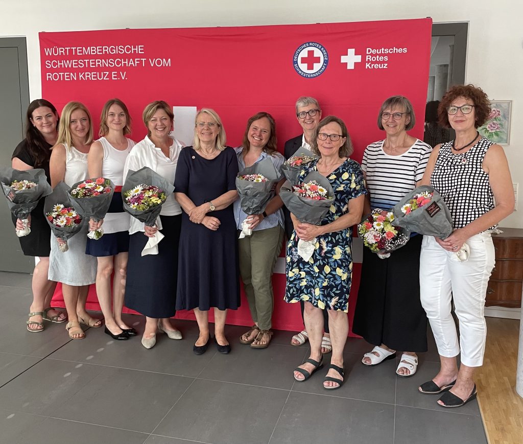 Neu gewählter Beirat vor Fotowand der Württembergischen Schwesternschaft mit Bluemensträußen
